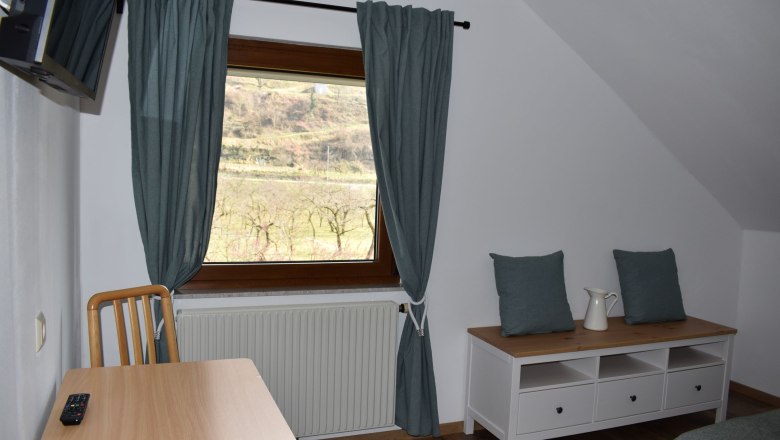 View from the room, © Familie König Interior view of a room with window, table, chair and chest of drawers.