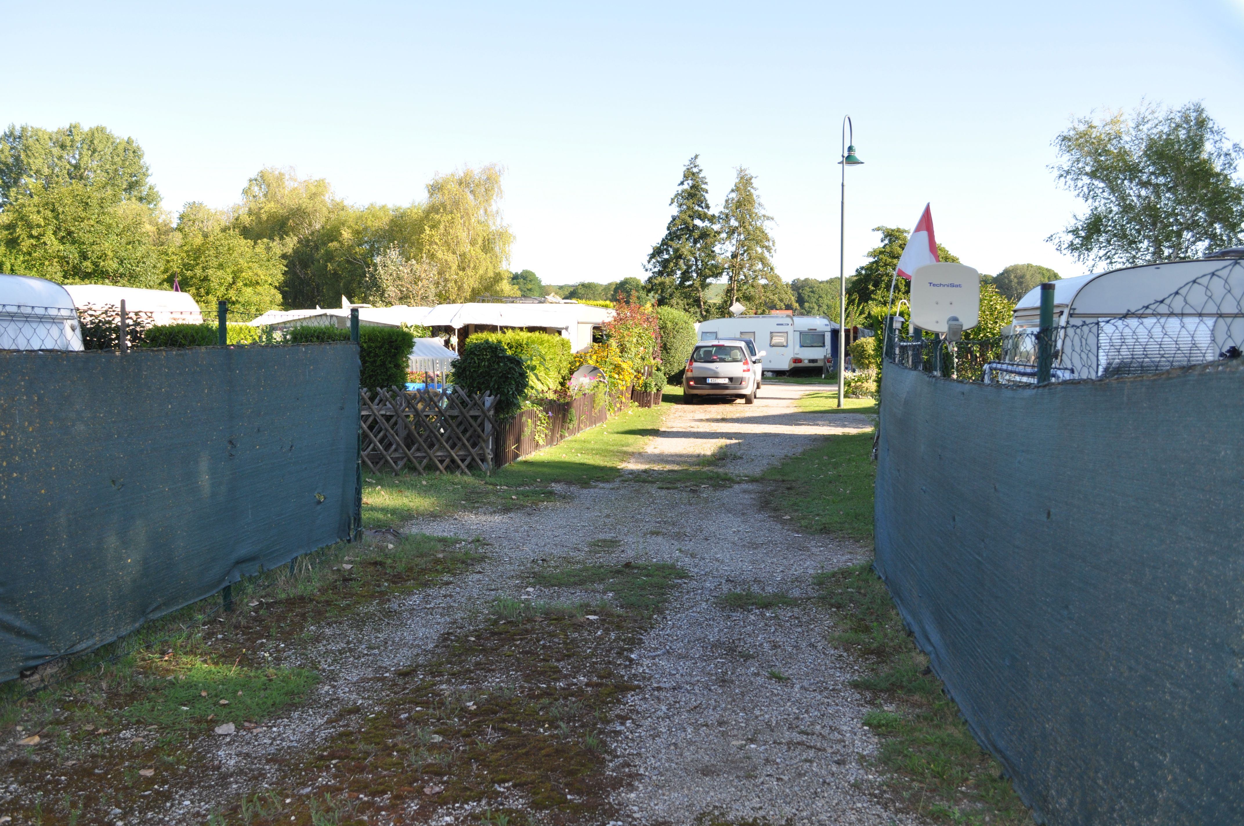 A campsite with caravans and a car on a gravel road, surrounded by trees and fences.