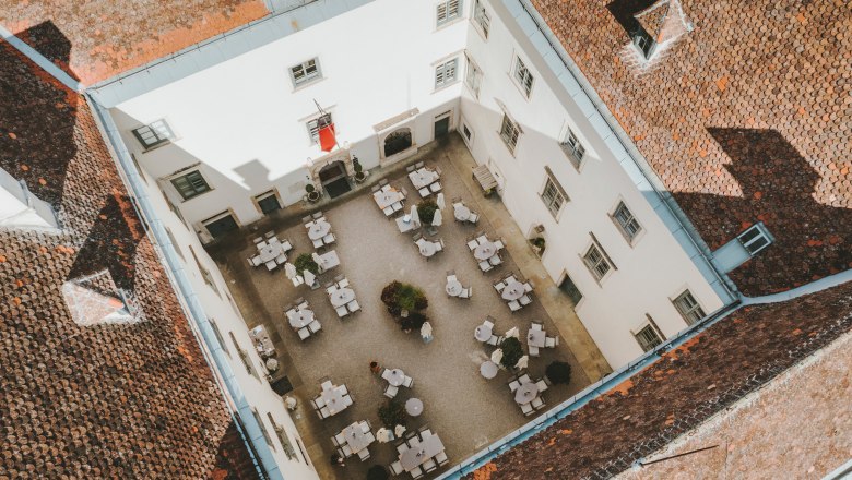 Aerial view of an inner courtyard with tables and chairs, surrounded by a building with red tiled roofs.