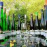 A selection of wine bottles and a wine glass on an outdoor table surrounded by green vegetation.
