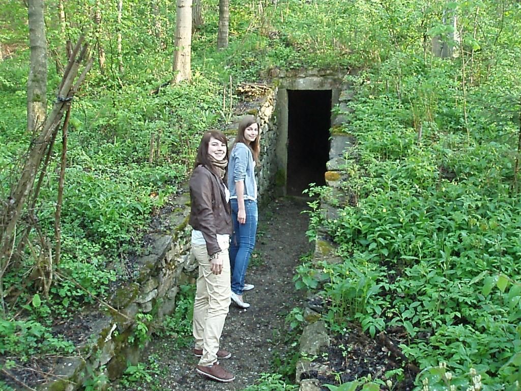 Two people are standing in front of an old ice cellar in the forest.