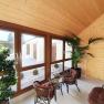 Interior view of a veranda with wooden walls, large windows, plants and rattan furniture.