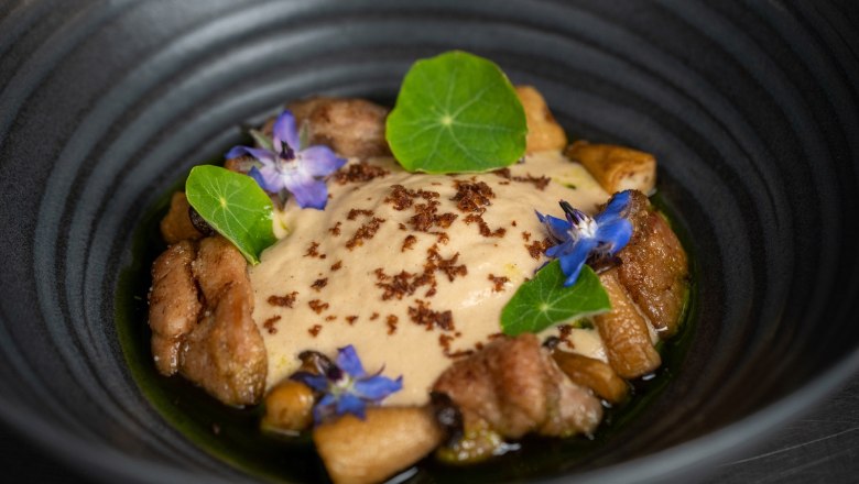 An elegant dish in a black bowl, decorated with edible flowers and green leaves.