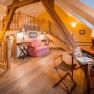 Cozy attic suite with wooden beams, sofa, desk and stairs to a sleeping area.