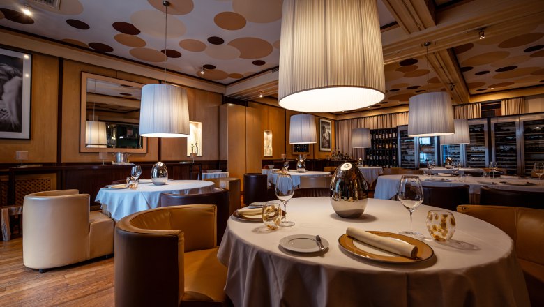 Elegant restaurant with round tables, white tablecloths and large, hanging lamps.