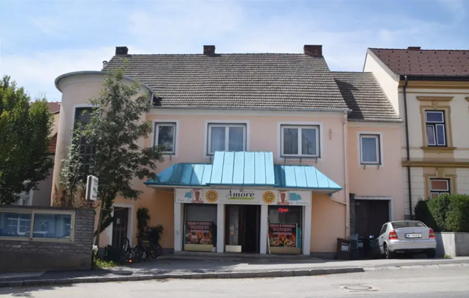 A small restaurant with a blue awning and a car in front of it.