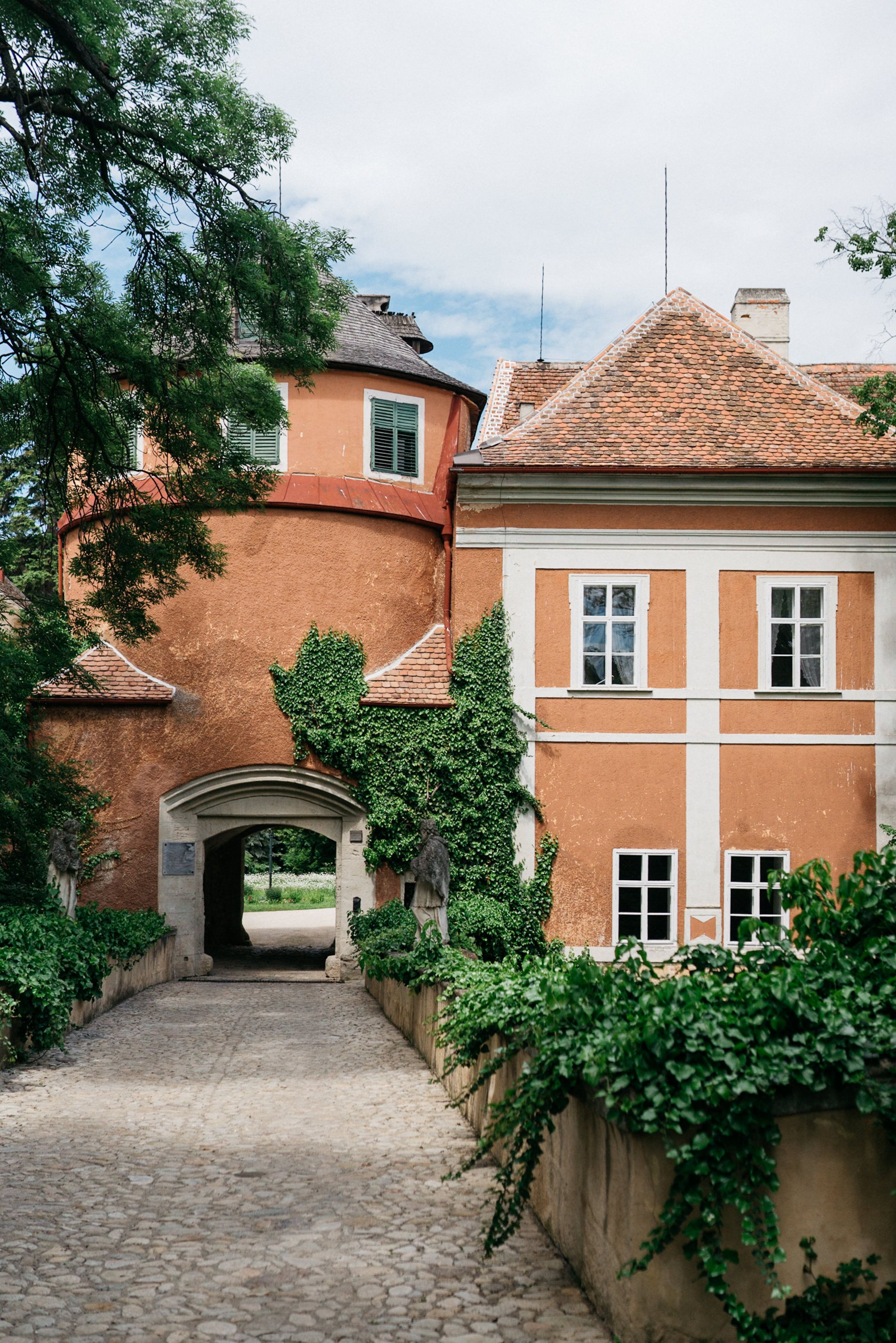 Entrance gate to Schrattenthal Castle with overgrown façade and paved path.