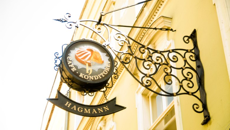 Metal sign 'Caf&eacute; Konditorei Hagmann' on a yellow house wall.