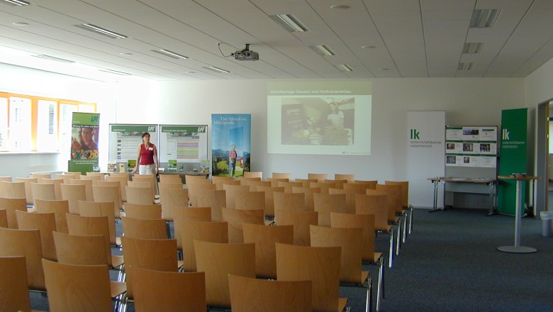 An empty seminar room with wooden chairs, a screen and advertising banners.
