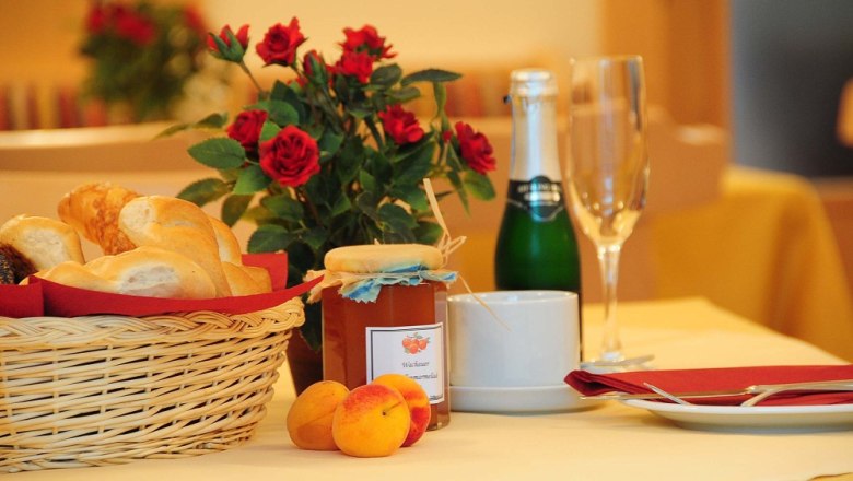 Breakfast table with bread basket, jam, champagne bottle and roses.