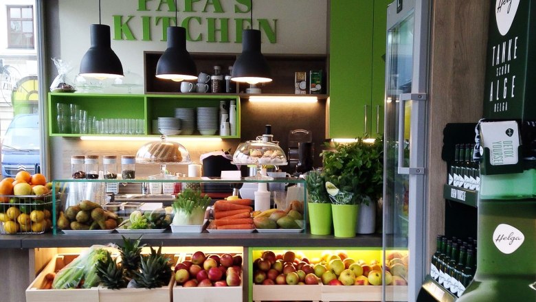 Interior view of a modern restaurant with fresh fruit and vegetables, green decoration and the lettering ‘Papa's Kitchen’.