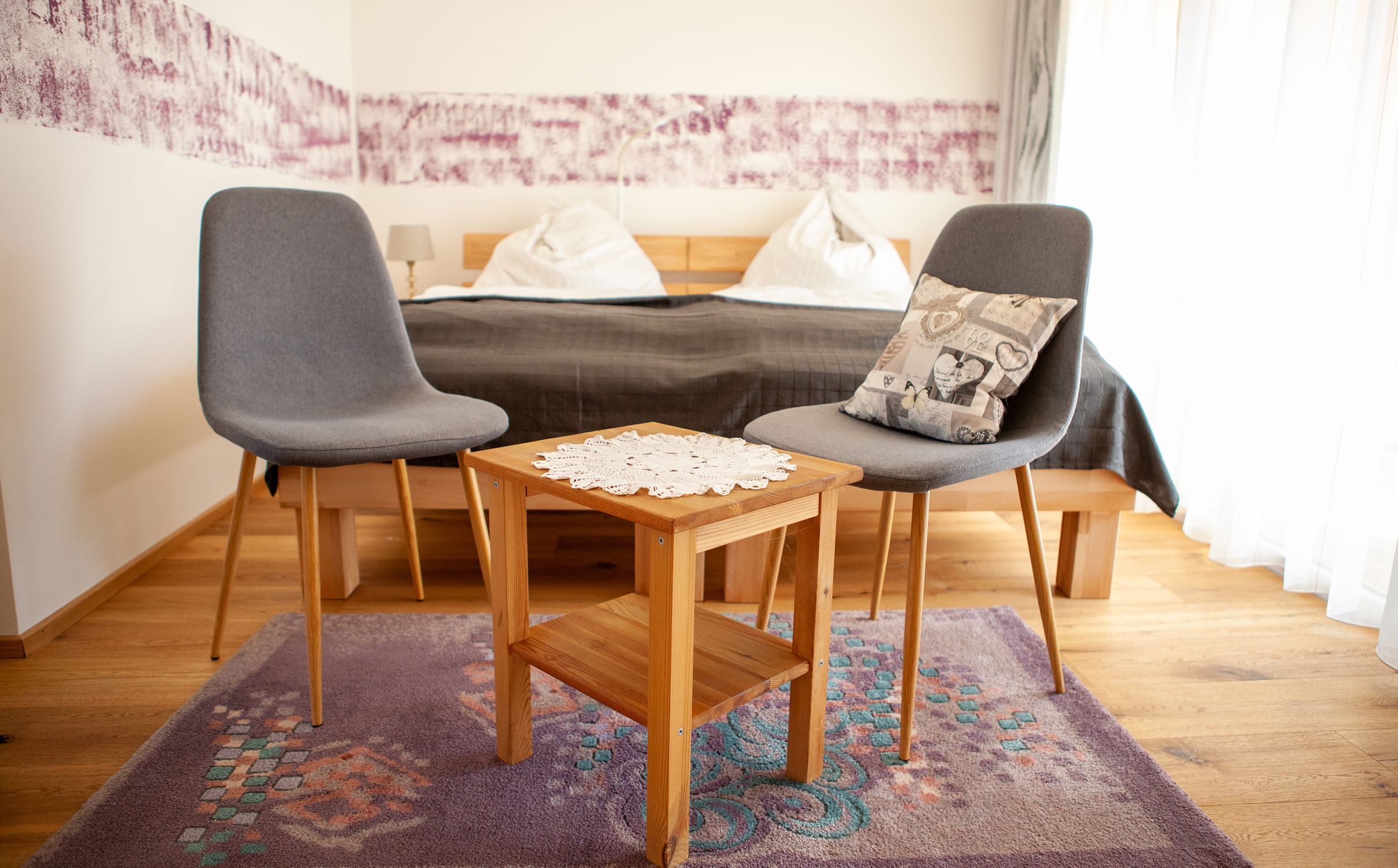 Two gray chairs and a wooden table with a doily in a bedroom.