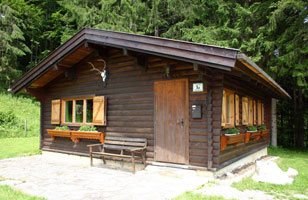 Hunting lodge, © Archiv A small, rustic wooden hunting lodge with shutters and antlers on the façade, surrounded by forest.