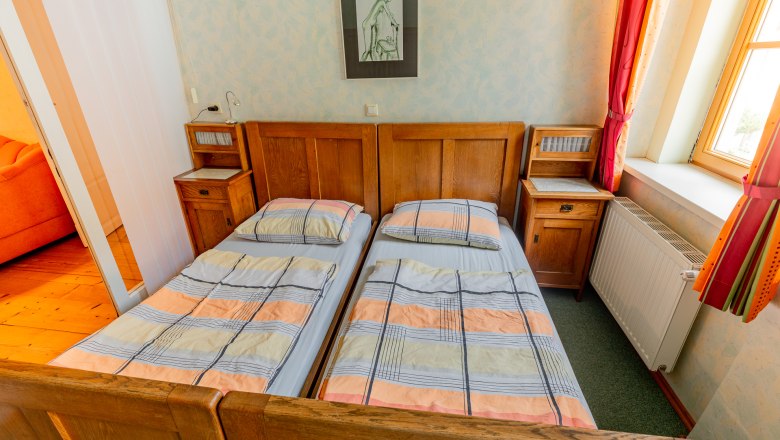 A bedroom with two single beds, wooden furniture and a window with red curtains.