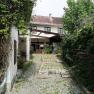Paved courtyard entrance with plants and a white building in the background.