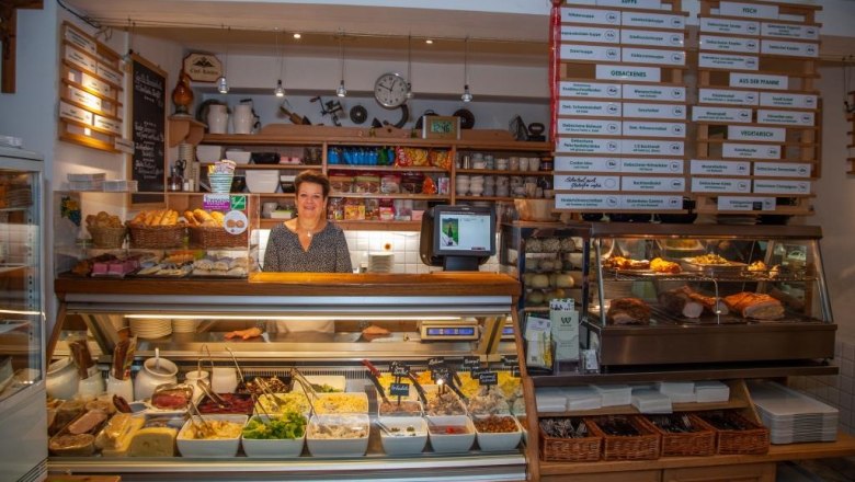 Woman behind a buffet with various dishes in a restaurant.