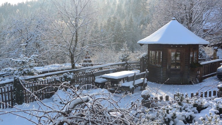 Snowy landscape with wooden hut, wooden fence and forest in the background.