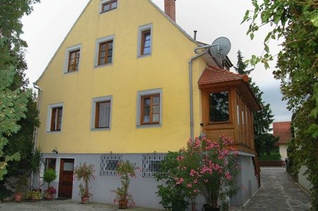 Exterior view of the Weiss guest house, © Fam. Weiss Yellow guest house with wooden veranda and flowering plants.