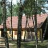 A yellow building with a red tiled roof, surrounded by birch trees in the forest.