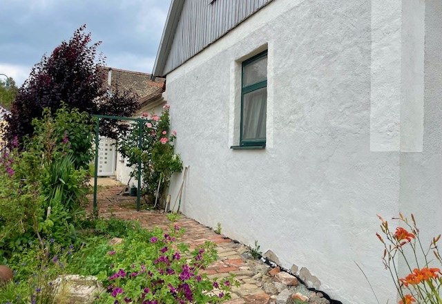 Exterior view of a house with a white wall, garden and flowers.