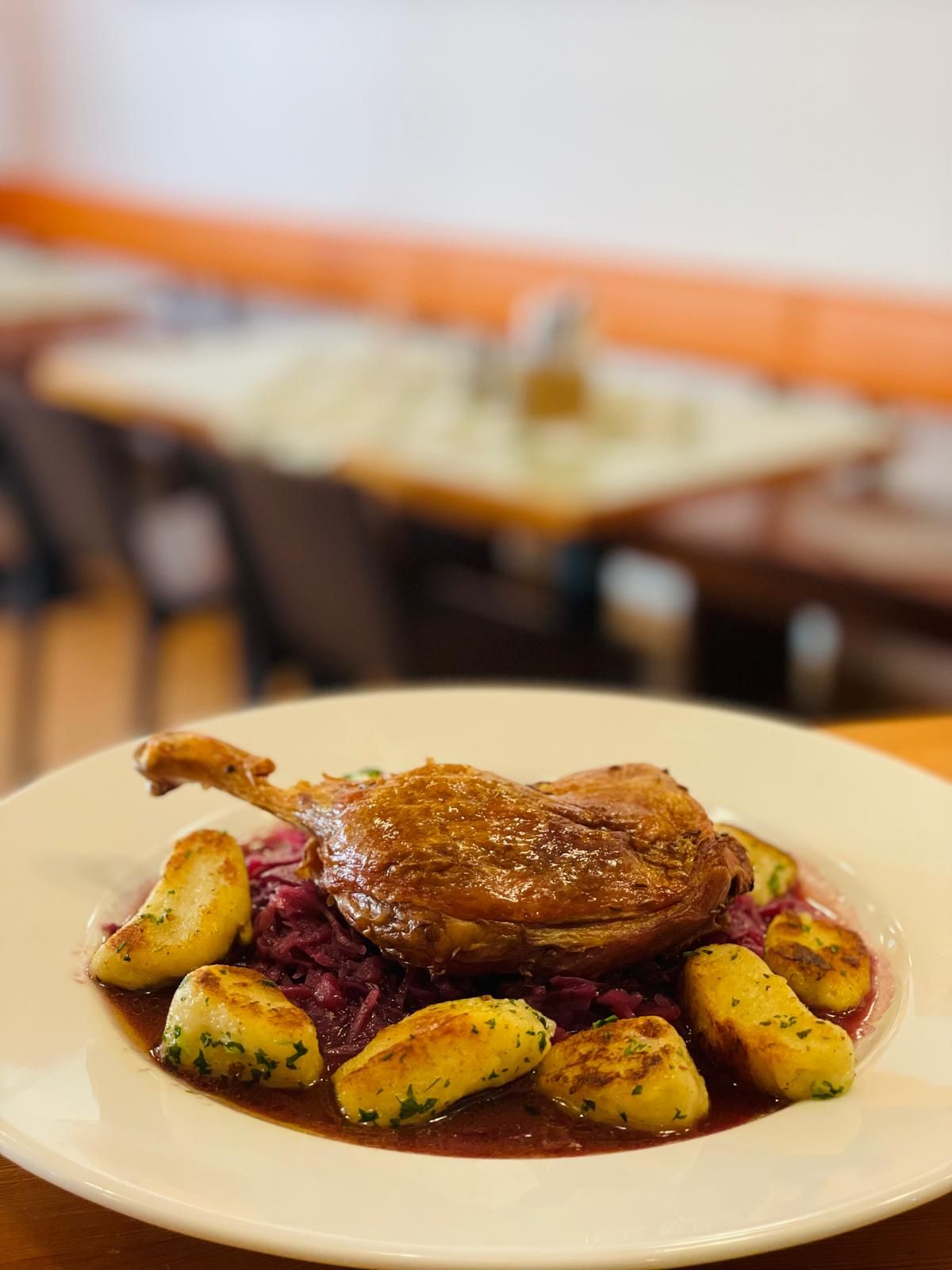 A plate of roasted duck leg, potato dumplings, and red cabbage at a restaurant.