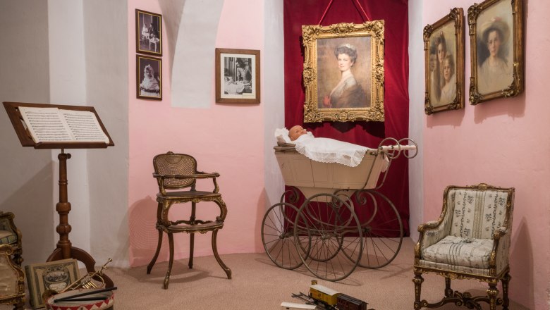 Historic children's room in the museum with antique baby carriage, chairs and toy train.
