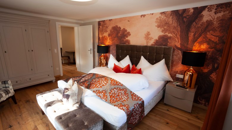 Elegant suite with large bed, decorative pillows and stylish wallpaper in Schloss Luberegg.