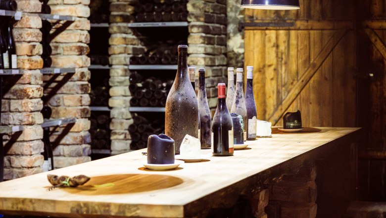 A wine cellar with brick walls, shelves full of wine bottles and a wooden table with several bottles of wine on it.