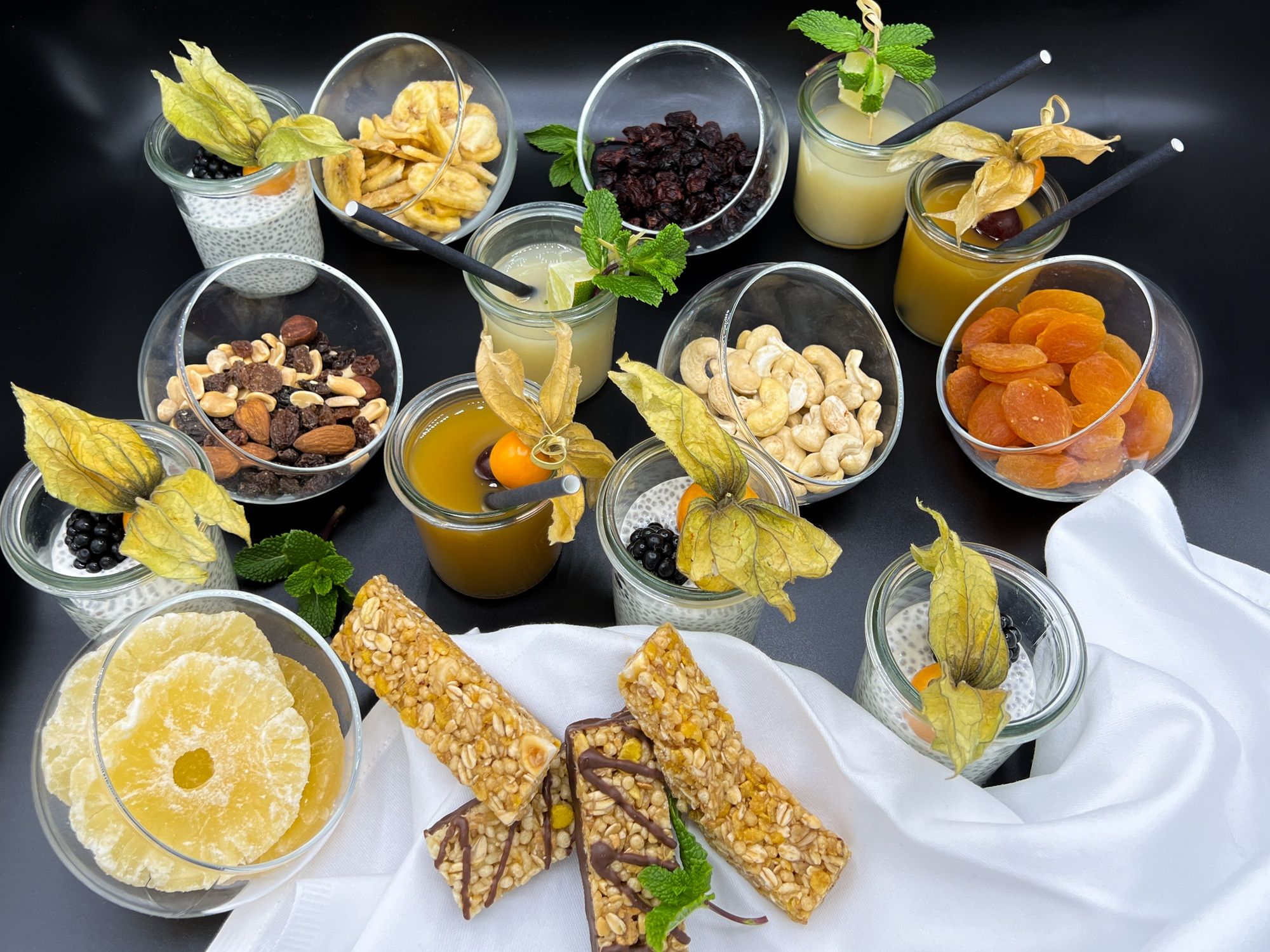 A selection of snacks and drinks, including nuts, dried fruit, chia pudding, and juices, arranged on a table.