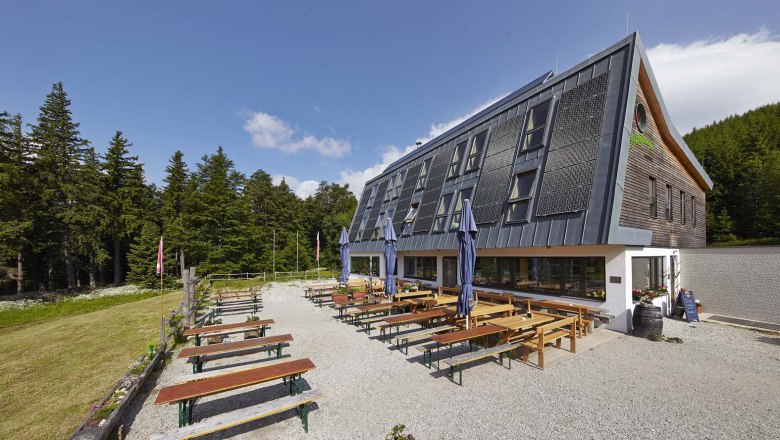 A modern building with solar panels and an outdoor beer garden surrounded by forest.