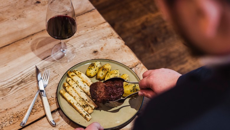 A plate with fillet of beef, asparagus and potatoes, next to a glass of red wine on a wooden table.