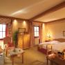 Cozy country-style hotel room with double bed, sofa, table and rustic wooden furniture.