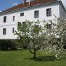 A white building with a brown roof and blossoming trees in the foreground.