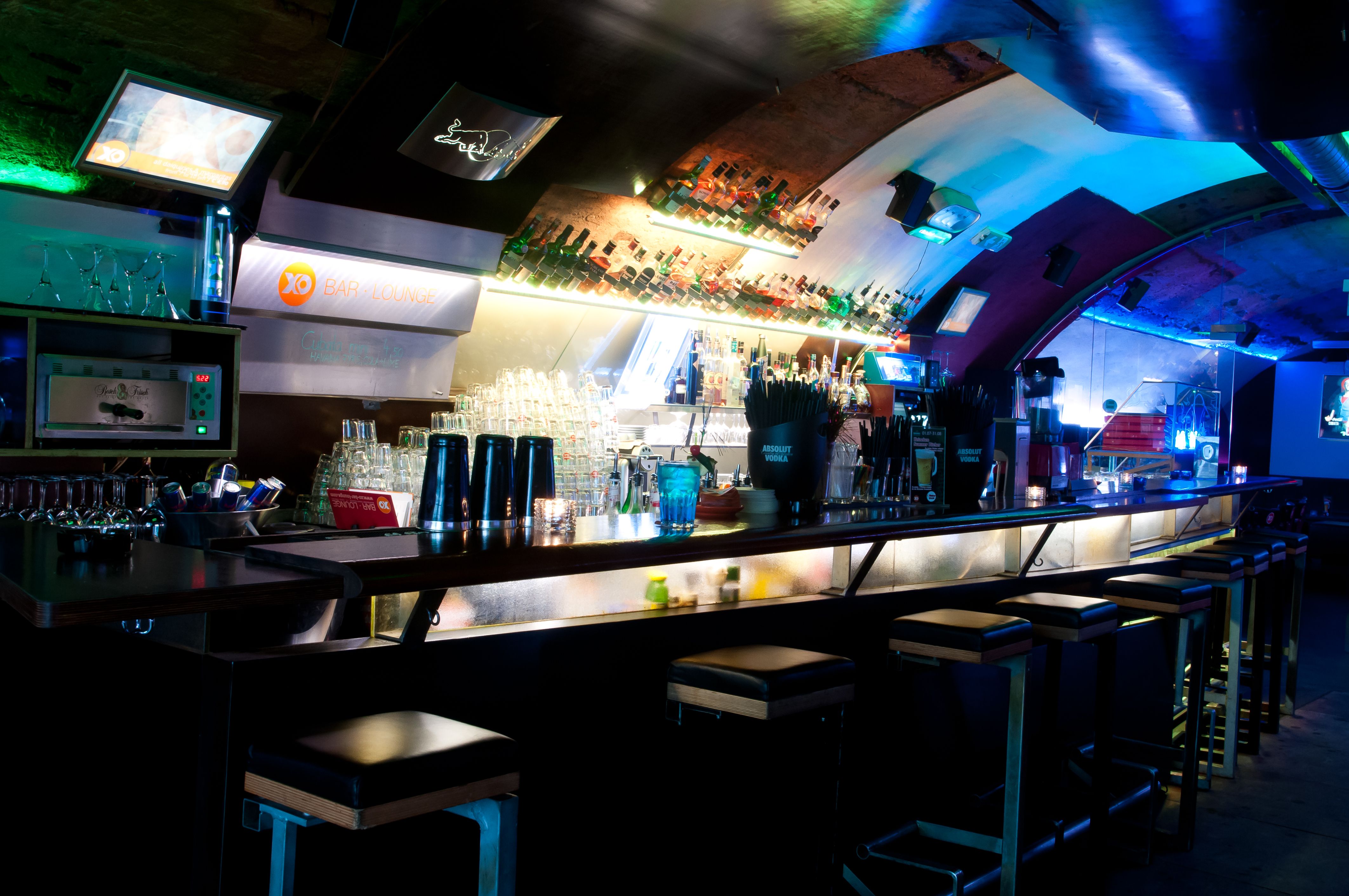 Interior view of a stylish bar with illuminated counter and bar stools.