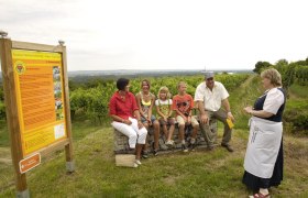 Group of people sitting on crates next to a sign on a vineyard.