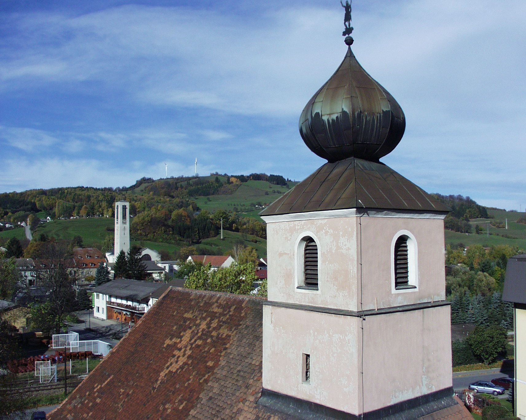 Church tower with onion roof in front of a hilly landscape and wind turbines.
