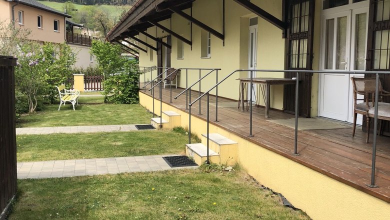 Exterior view of a yellow building with veranda and mountain in the background.