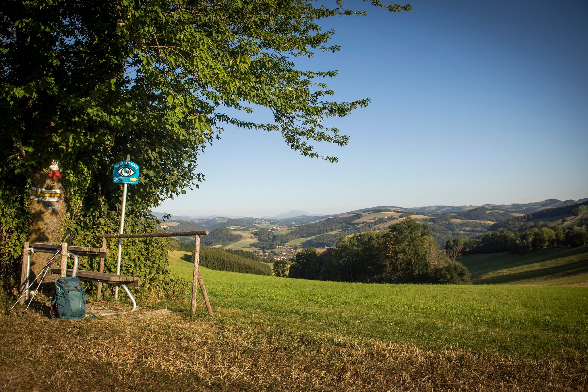 Landscape with bench, walking stick and rucksack in the foreground, hills and mountains in the background.