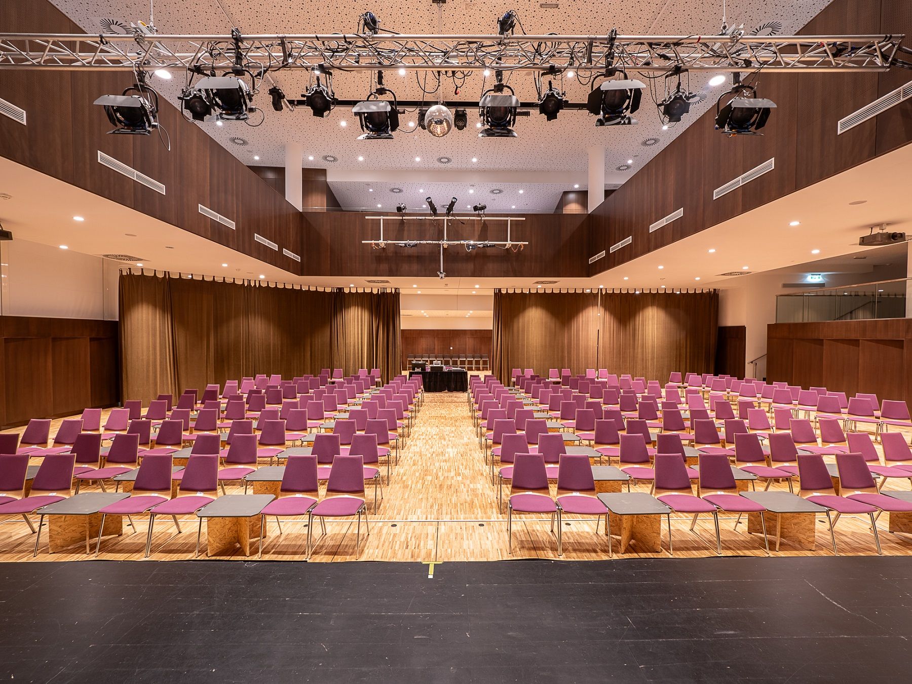 Interior view of an empty event room with purple chairs and wooden floor.