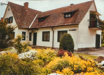 House Birgit, © Hedi Kienberger A white house with a red tiled roof and a garden full of yellow flowers.