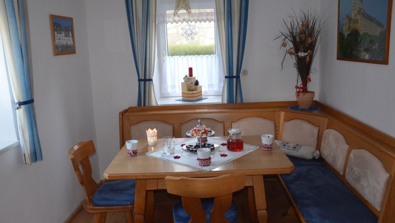 Cozy dining room with wooden table, corner bench and blue upholstery. Window with blue curtains and Christmas decorations.