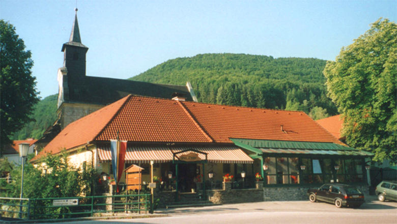 A country inn with a red roof in front of a wooded hill.