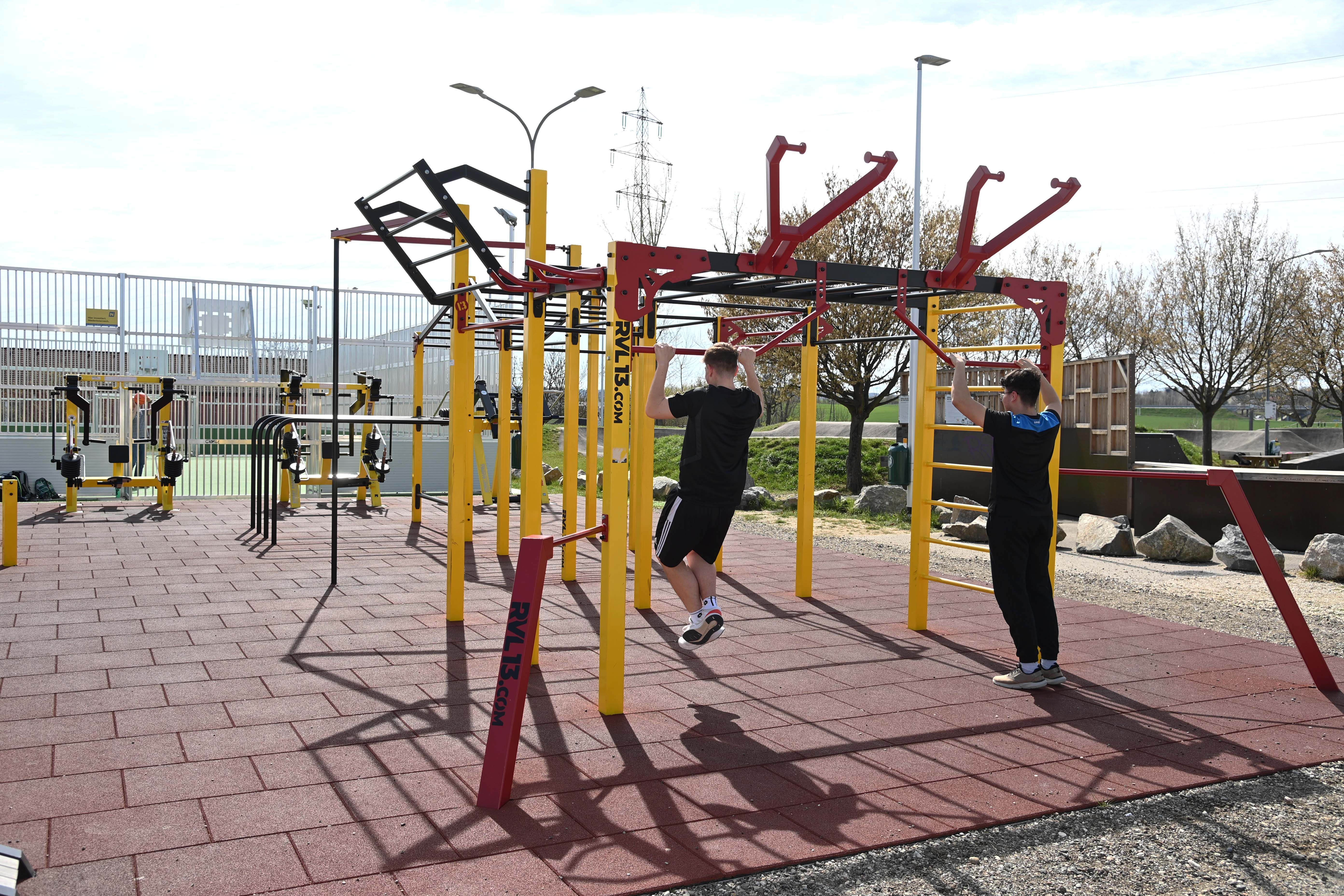 Two people train on a calisthenics scaffold outdoors.