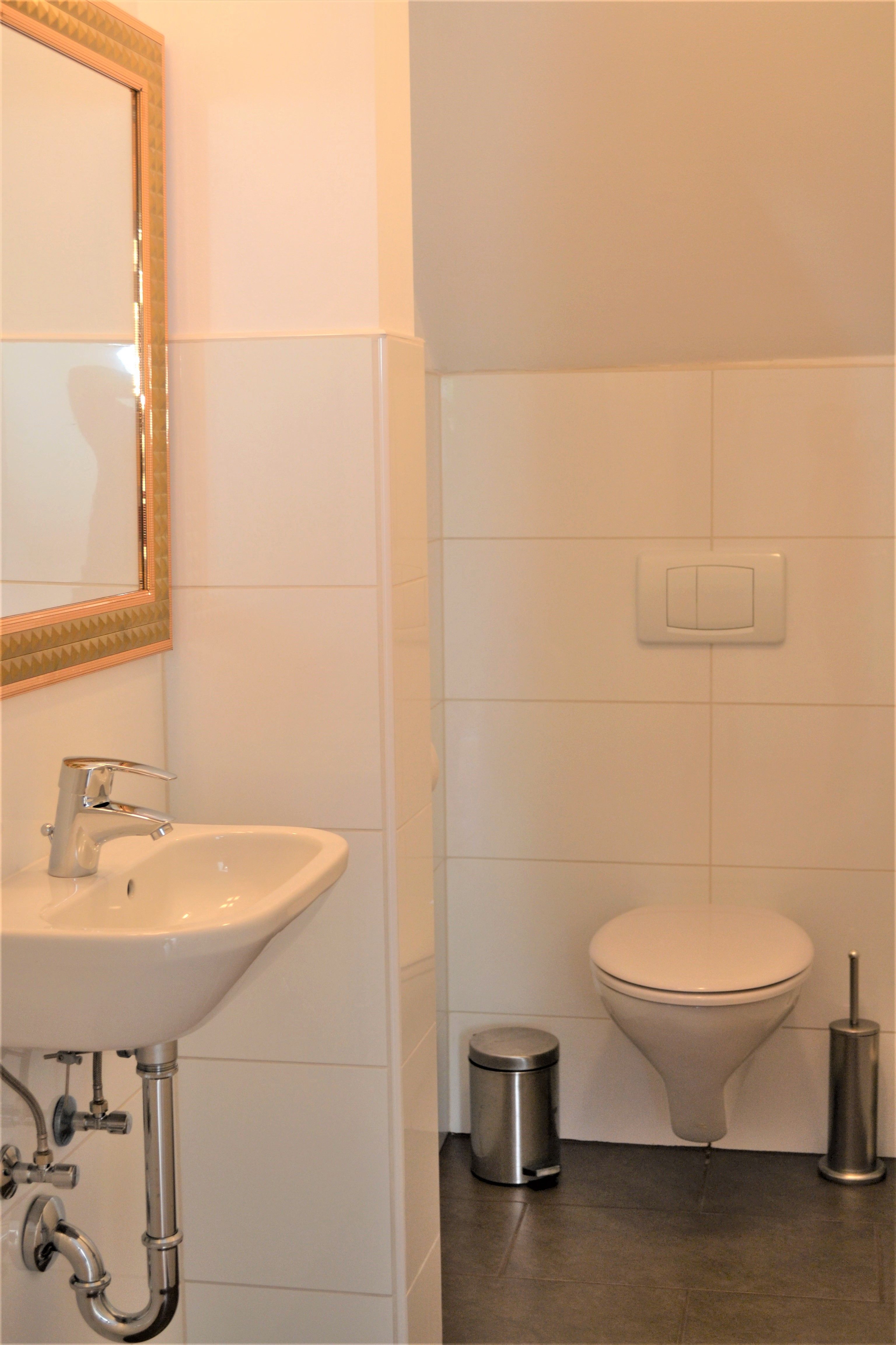 Small bathroom with washbasin, mirror, toilet, waste garbage can and toilet brush.