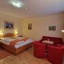 Hotel room with double bed, red sofa and armchairs, wooden floor and murals.