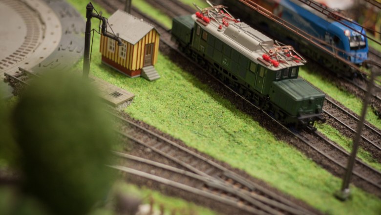 Model railroad with green train and small building on a layout.