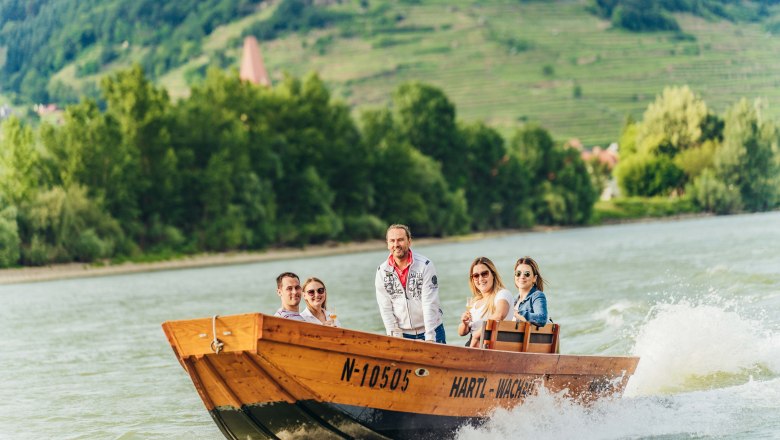 Group of people on a wooden boat on the Danube with a green landscape in the background.