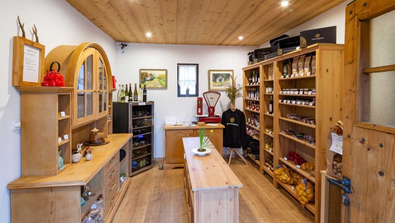 Interior view of a small, cozy store with wooden shelves filled with regional products such as wine, jam and vegetables.