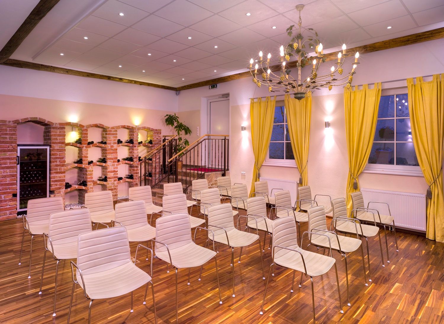 A conference room with white chairs, yellow curtains and a chandelier.
