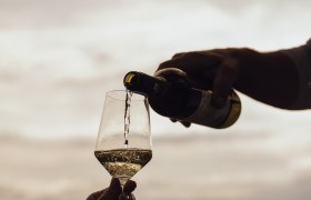 Wine is poured into a glass outdoors, with a landscape in the background.